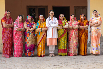 Concept of Rural Health in India. Indian rural women arm crossed while standing with young female doctor in rural courtyard shelter village, Rural India healthcare 