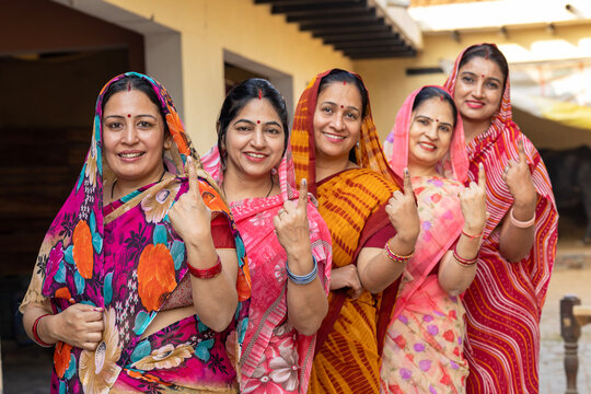 Group of happy rural indian women standing in queue showing their finger marked with black ink after casting vote. Election in india.