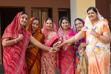 A group of Indian hindu women join hands in colorful traditional dresses posing in front of the...