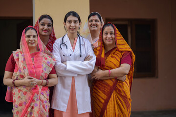 Concept of Rural Health in India. Indian rural women arm crossed while standing with young female doctor in rural courtyard shelter village, Rural India healthcare 