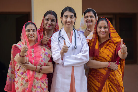 Concept of Indian rural women health care in India. Indian female doctor standing showing thumbs up with group of rural women rural health camp at village. Protection of cervical cancer 