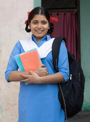 Portrait of Happy Rural Indian student school girl wearing blue government school uniform holding...