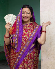 Indian happy rural village woman showing Indian 500 notes currency by looking at camera - concept...