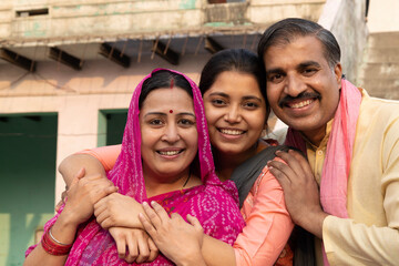 A rural Indian family of a Father and a Daughter embracing outdoor Daughter holding note books, looking at camera while father blessing to her daughter in a village having a good time together