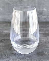 A simple, clean image of a glass tumbler filled with water, resting on a neutral gray backdrop, highlighting the transparency of the glass