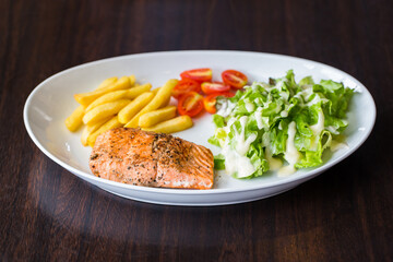 Grilled salmon steak with french fries tomatoes and vegetables