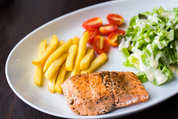 Grilled salmon steak with french fries tomatoes and vegetables