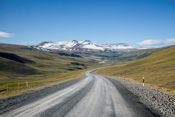 Winding gravel road through a valley, snow-capped mountains in the distance