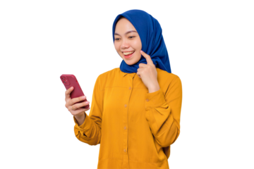 Smiling young Asian Muslim woman dressed in orange shirt looking at mobile phone screen, feels joyful reading good news isolated on transparent background