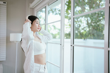 Fototapeta premium beautiful Asian woman sits in a cozy living room, wearing headphones, enjoying music, feeling carefree, joyful, relaxed and free.