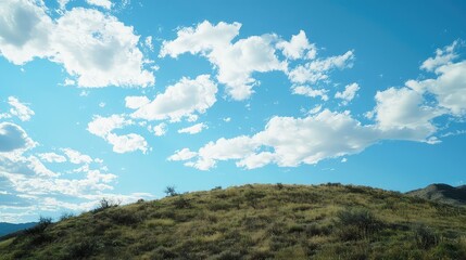 Obraz premium Vibrant Blue Sky with Fluffy White Clouds over Lush Green Hilltop Landscape in Bright Sunlight Serene Outdoor