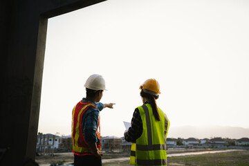 Engineers and architects collaborate at a construction site, wearing safety gear, examining blueprints, discussing plans, ensuring teamwork, development, and safety.