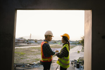 Engineers and architects collaborate at a construction site, wearing safety gear, examining...