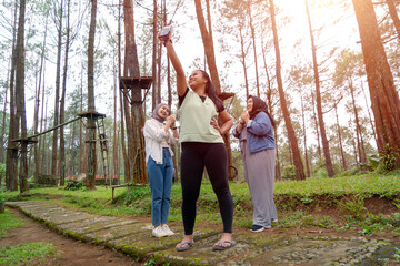 Fototapeta premium Three Young Asian Indonesian Women Taking Selfie in Forest During Outdoor Adventure