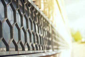 Metal hexagonal honeycomb grille on a tall sunlit window, creating striking geometric shadows and...