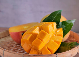 A ripe, juicy mango artfully presented on a woven bamboo tray. The mango is cut open, one half scored into neat, cube-like sections, slightly pushed outward to showcase the vibrant orange flesh.