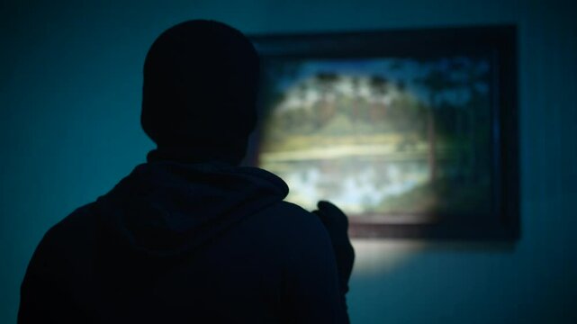 A robber examines a painting before stealing it