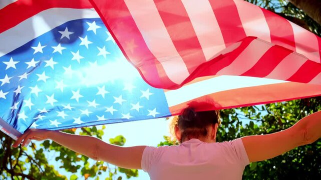 A woman holds USA flag against a strong wind, with a background of clear blue sky, sea and tropical trees.