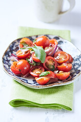 Simple salad with cherry tomatoes, red onion and fresh herbs. Bright wooden background. Close up.