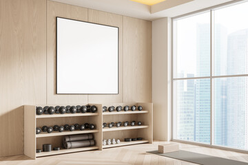 Modern gym interior with blank poster mockup on light wooden wall, dumbbells on shelves, and yoga accessories near panoramic windows in cityscape background. 3D Rendering