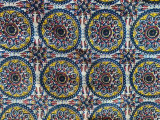 This white cotton fabric showcases a delicate all-over floral mandala pattern in vibrant shades of blue, pink, and yellow.