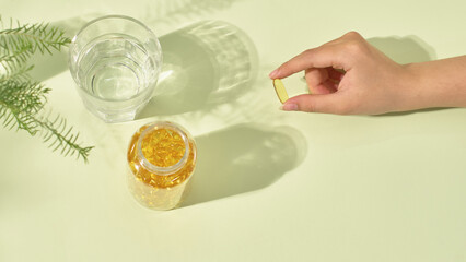 Top view of an open drug bottle, containing hundred golden pills. Each pill is about a finger's length, held carefully between the index finger and thumb. Minimalist layout, medicine concept.