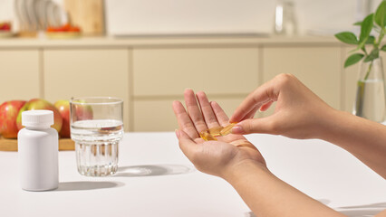 Patient is taking the pills in hand to take. A glass of water is placed on the table. In the...