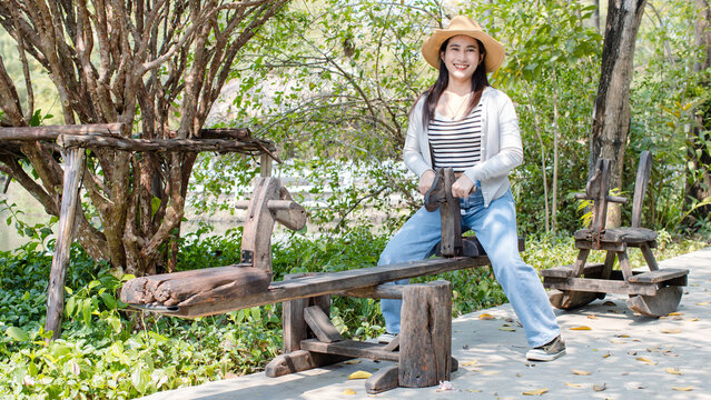 Asian beautiful women cheerful enjoying sunny day outdoors sitting on rustic wooden seesaw in green park wearing straw hats and casual outfits smiling look at camera, concept relax weekend lifestyle.