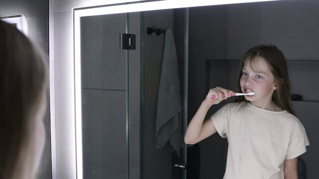 A little girl brushes her teeth before going to bed in front of the bathroom mirror