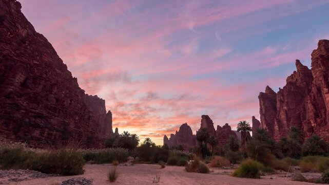 Timelapse of sunrise to sunset over dramatic rock formations in Wadi Disah, Saudi Arabia. Vibrant sky transitions cast dynamic light on towering cliffs, canyons, and desert terrain. 