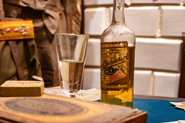 A Glass of Golden Liquid Alongside an Old Bottle with Vintage Label on a Desk