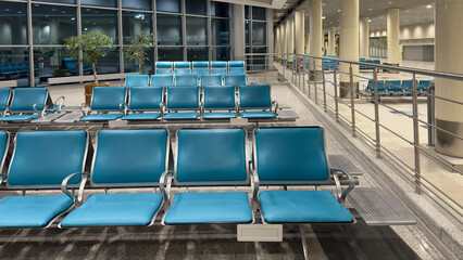 Spacious airport waiting area with empty chairs facing large windows. Empty waiting chairs in the airport building in the evening.
