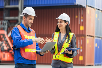 Female foreman safety vest using clipboard checklist and Engineer man in hardhat holding laptop for control loading containers box from cargo