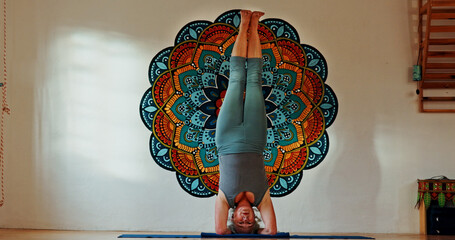 Balance, upside down or yoga and woman in studio with wall art for fitness or wellness routine. Exercise, headstand or pilates and senior person in class with mandala symbol for holistic health