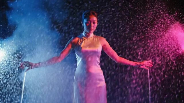 Dark silhouette of exotic dancer on a smoky background in a dark studio. A woman dances seductively among the raindrops in an oriental dress. Slow motion. Close up