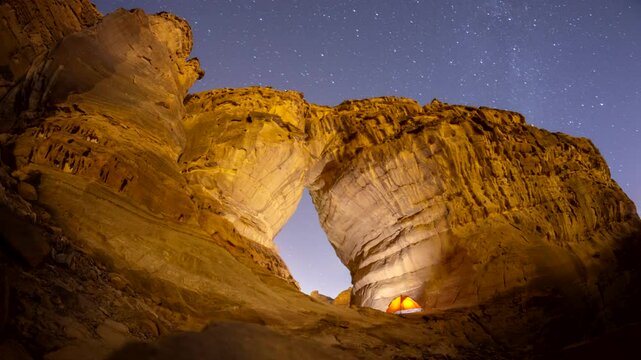 Time lapse of night stars motion while camping tent at bottle shape rock formation near elephant rock in Alula, Madinah, Saudi Arabia