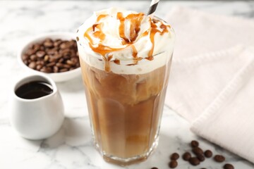 Tasty iced coffee with whipped cream, syrup and beans on white marble table, closeup