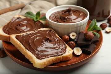 Toasts with chocolate hazelnut spread, nuts, pieces of chocolate and mint on white marble table, closeup