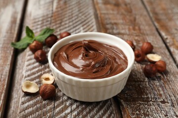 Chocolate hazelnut spread in bowl, nuts and mint on wooden table, closeup