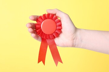 Woman holding red award ribbon on yellow background, closeup