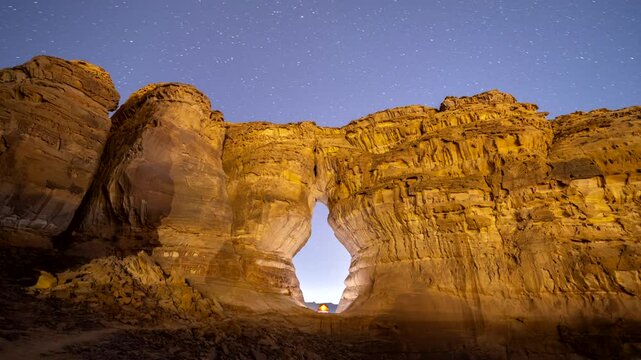Time lapse of night stars motion while camping tent at bottle shape rock formation near elephant rock in Alula, Madinah, Saudi Arabia