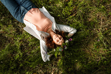 Woman with wildflower wreath lies on grass with closed eyes, sunlight