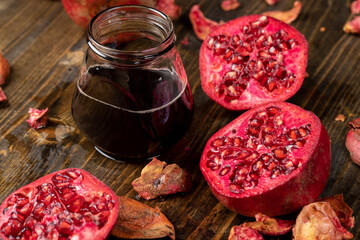 red pomegranate on a table and a jar of juice , red pomegranate cut into pieces next to natural pomegranate juice