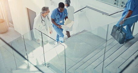 Paperwork, doctor and nurse walk on stairs with documents in hospital lobby. Above discussion,...