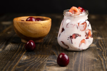 yogurt with cherry flavor and berry slices, glass jar with cherry yogurt with fresh red cherries, side view