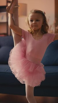 Smiling little girl in ballet tutu showing developpe pose, dancing at home