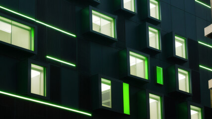 Obraz premium Modern Building Facade with Green Illuminated Windows at Night