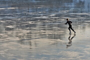 Girl learning ice-skating on frozen lake at sunset