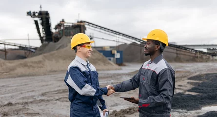 Gordijnen African and caucasian male engineers discussing in sand quarry mining site, industry of open mine © Parilov