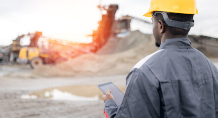 African male adult surveying engineer in sand quarry ore mining site with tablet computer. Concept...